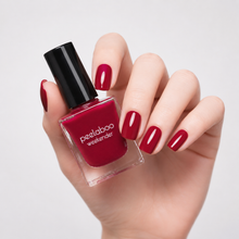 Load image into Gallery viewer, Hand holding a bottle of red nail polish with matching nails on a light gray background