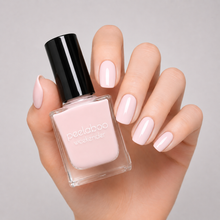 Load image into Gallery viewer, Hand holding a bottle of light pastel pink nail polish with matching nails against a gray background
